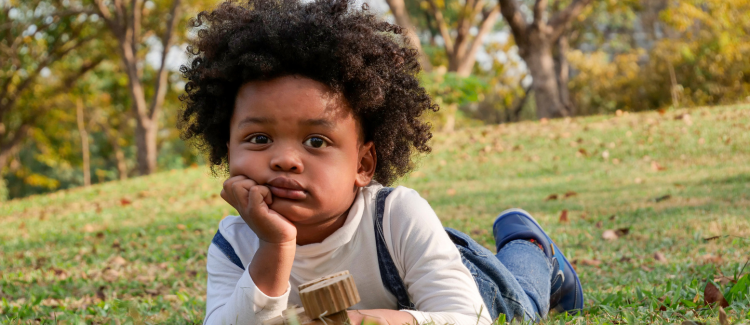 A young child bored, laying in the grass