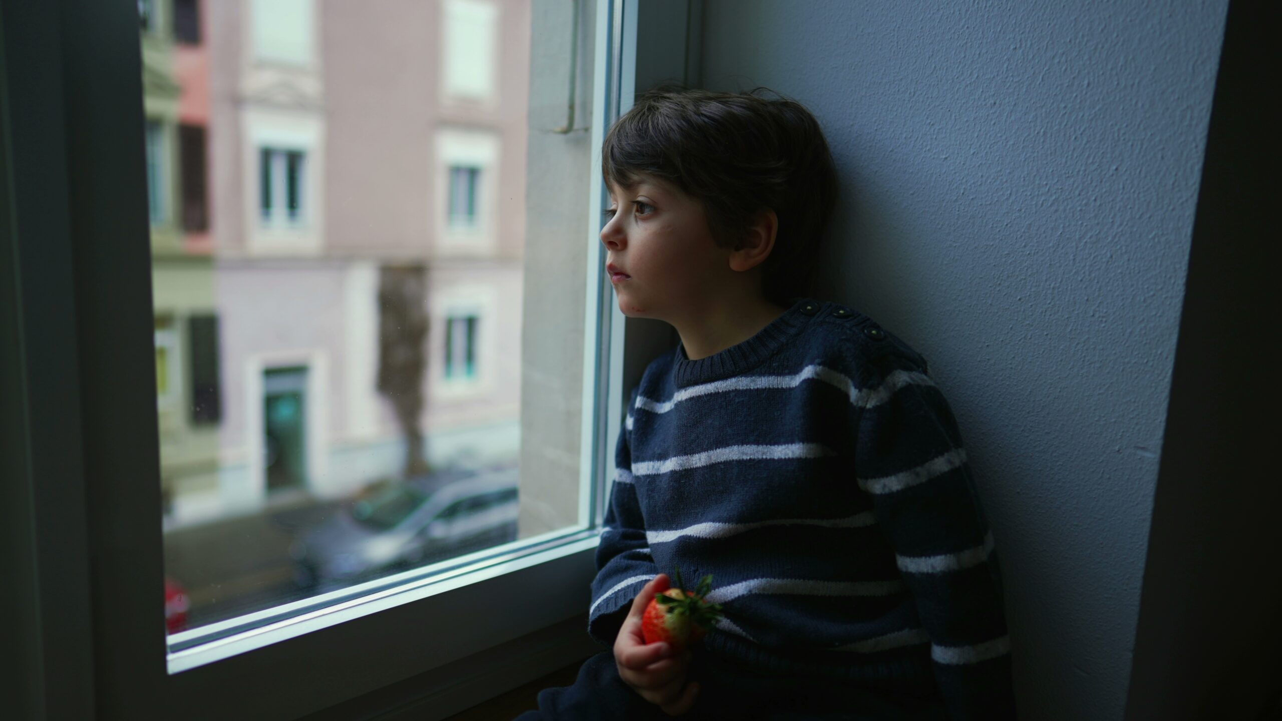 Young melancholy child looking out window.